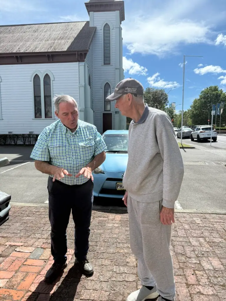 RJ Kost speaking with a local resident outside a church, highlighting community conversations and listening